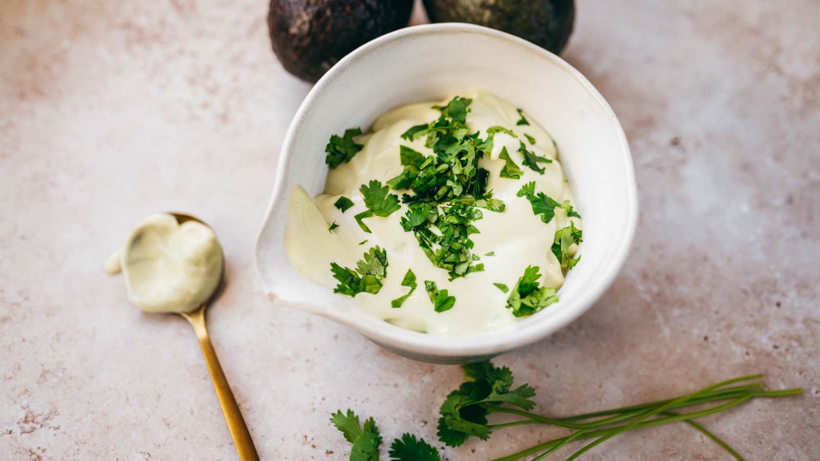 A small white ceramic bowl filled with a creamy green sauce garnished with fresh green cilantro leaves.