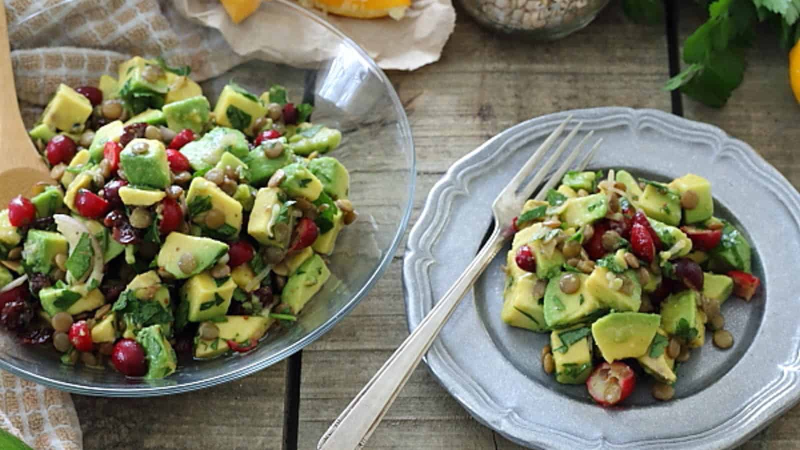Avocado lentil salad in a bowl with serving spoon and silver plate with fork.