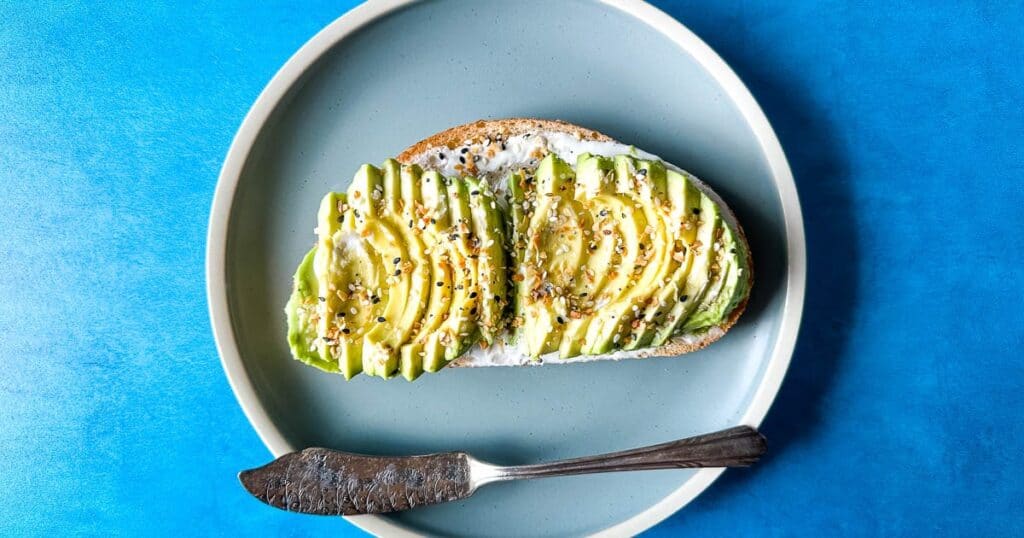 Finished avocado tartine with a vintage knife on a light blue plate on a medium blue background.