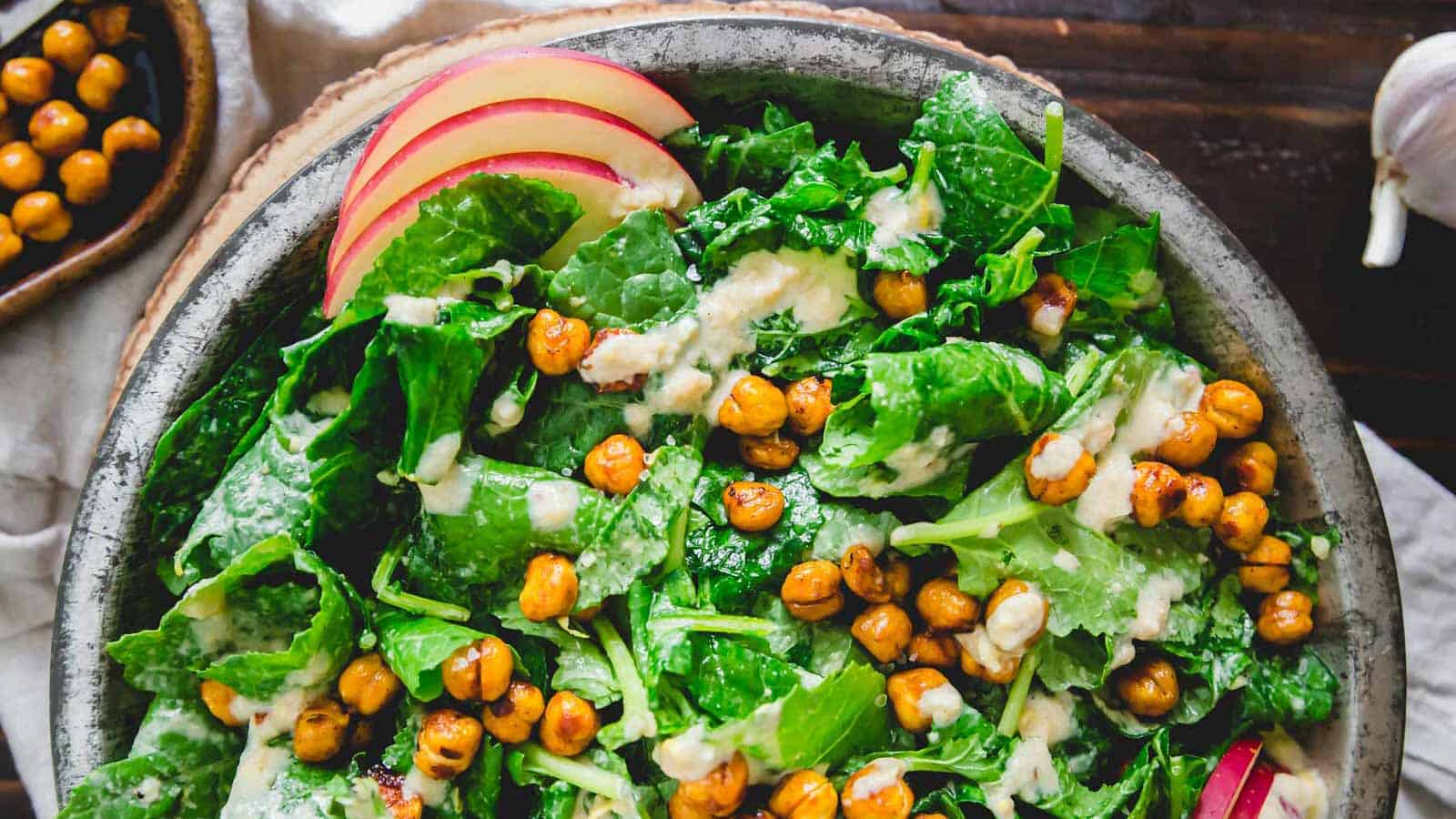 Baby kale salad in a metal plate with apples and roasted chickpeas.
