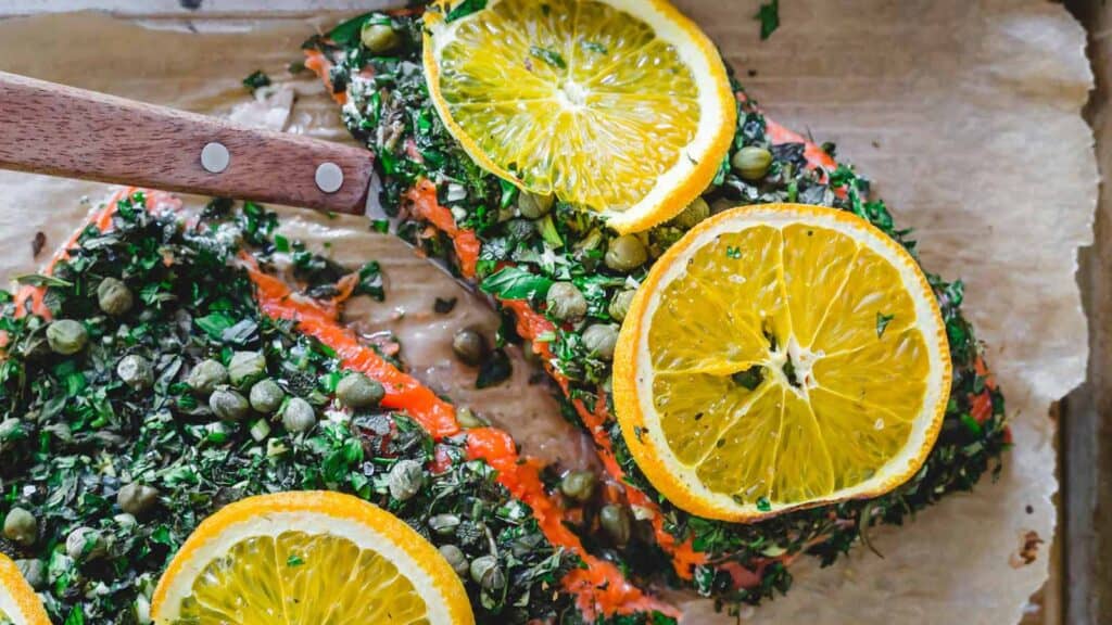 Baked sockeye salmon with herb caper crust and lemon slices on a sheet pan.