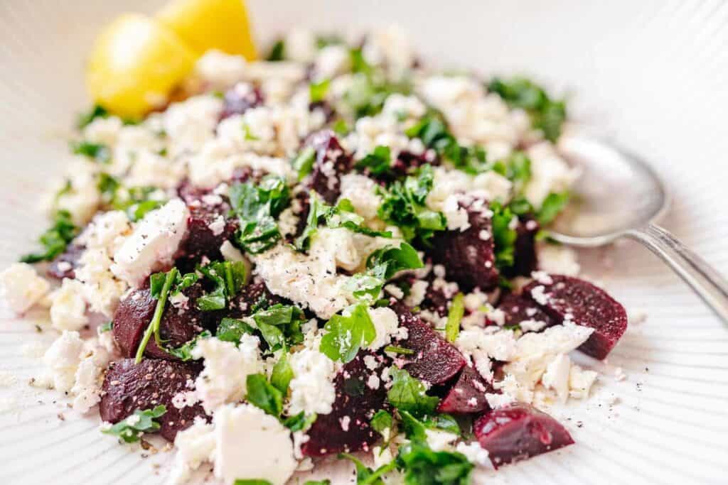 A large white ceramic bowl filled with chopped beets, frehs green herbs and white feta cheese.