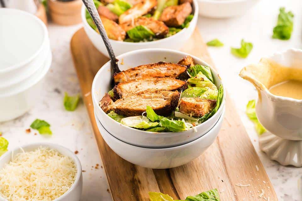 A chicken caesar salad in a white bowl on a table. 