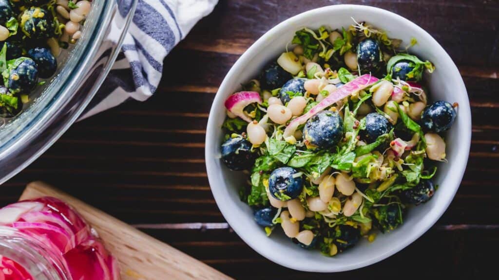 Blueberry white bean salad with tahini dressing in a white bowl with pickled onions in a jar to the side.