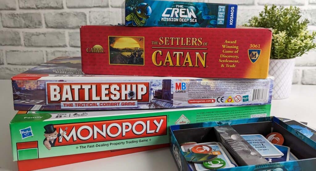 Stack of four board games, The Crew, Settlers of Catan, Battleship and Monopoly.