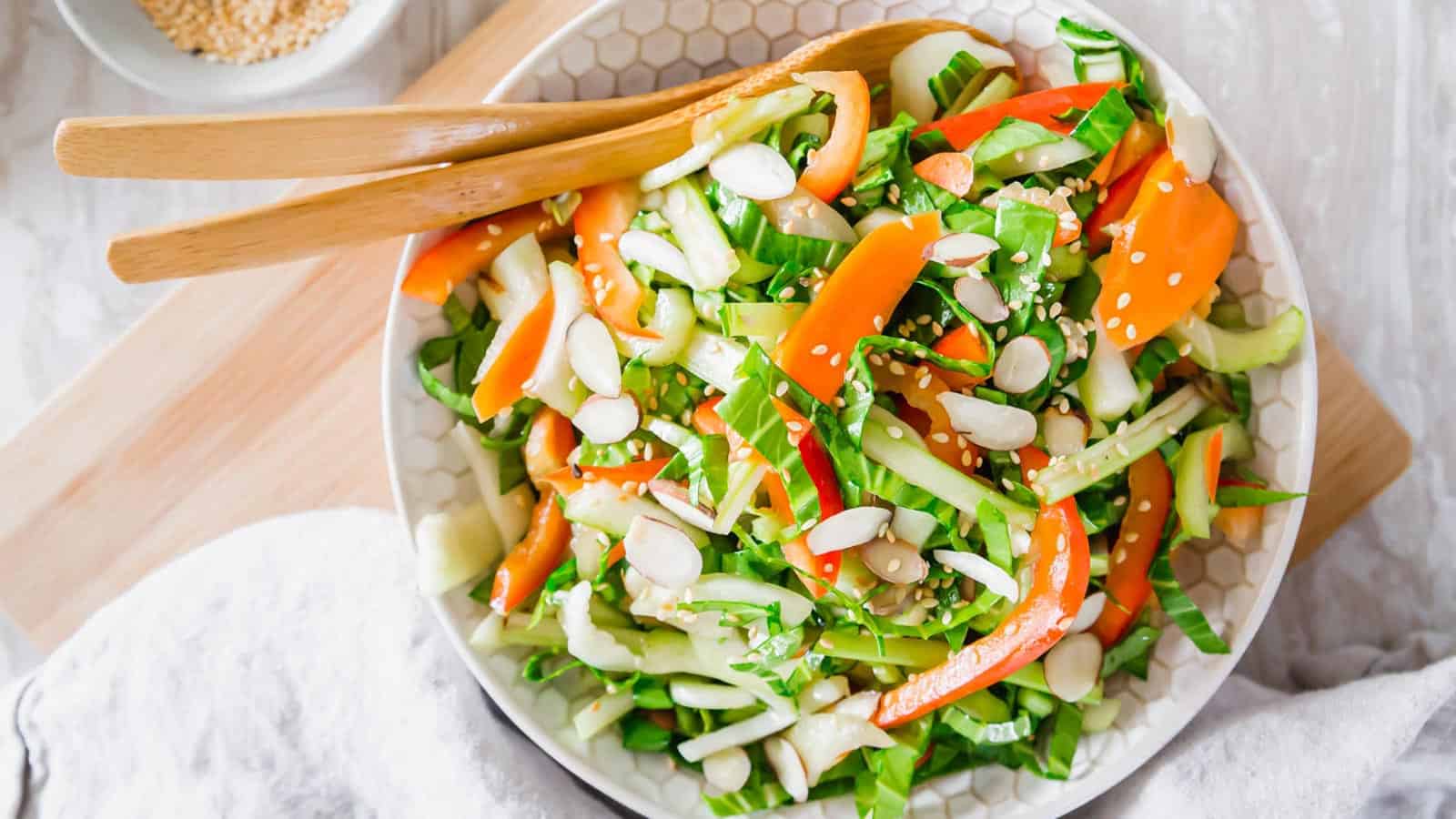 Bok choy salad with sesame dressing in a bowl with wooden serving utensils.
