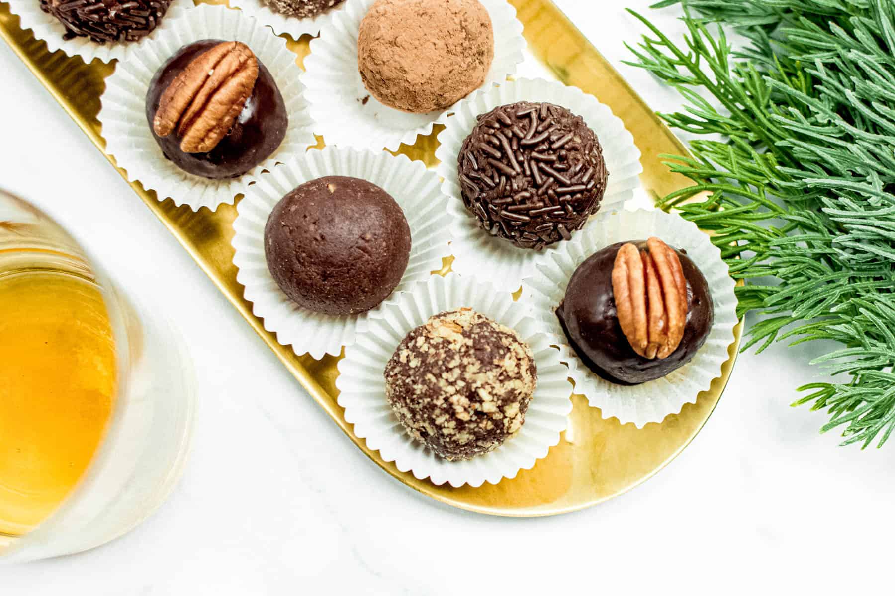 A tray of bourbon balls on a gold tray next to a glass of bourbon.