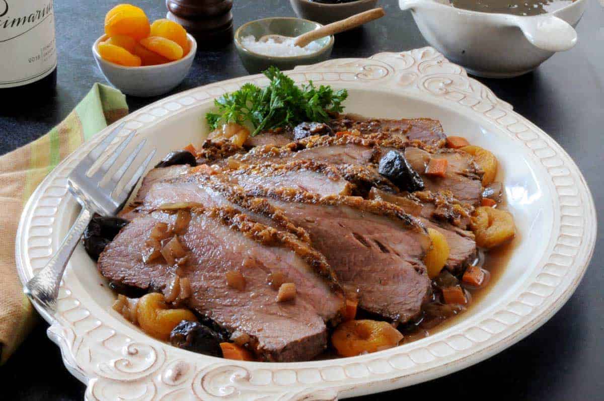 Low angle shot of sliced brisket on a white platter with dried apricots and salt in the background.