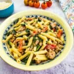 Broccoli Rabe and Sausage in a serving bowl with tomatoes in the background.