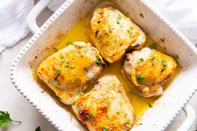 Easy Garlic Broiled Chicken Thighs with parsley in a white baking dish with a spatula.