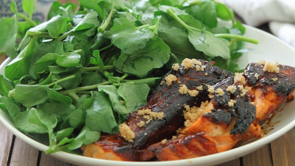 Brown sugar coated salmon filets served with baby greens on a plate.