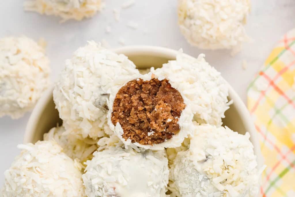 Carrot cake balls covered in coconut. One has a bite taken.