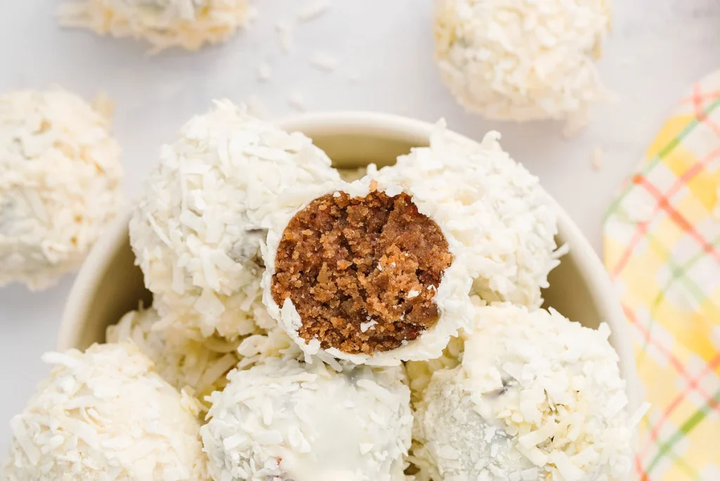 Carrot cake balls with a coconut coating. One has a bite taken.