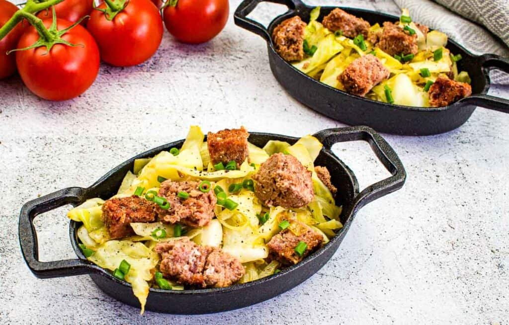 Canned Corned Beef and Cabbage in two black dishes with tomatoes in the background.