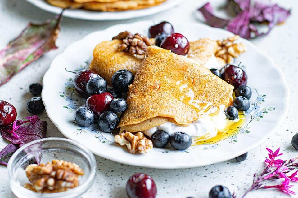 Crepes on a plate with fresh fruit and nuts on top.