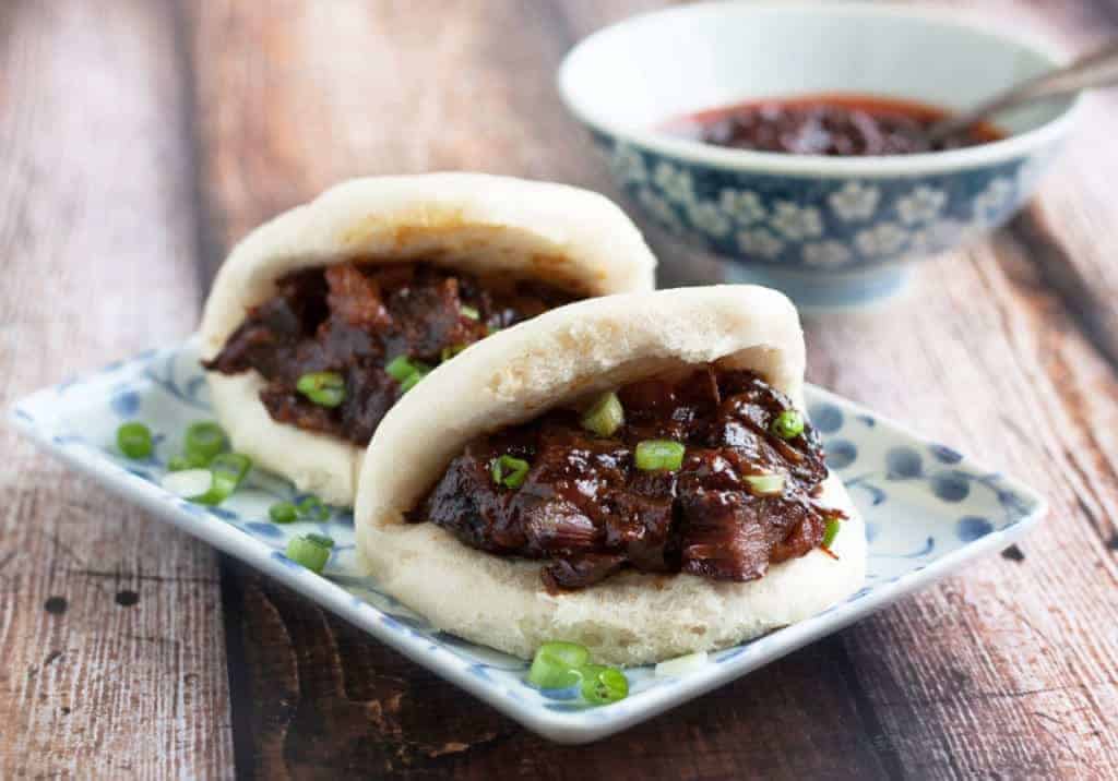 2 char siu bao on a plate with dipping sauce.