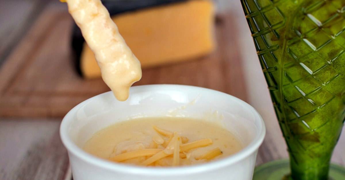 Gouda Cheese Sauce in a bowl with a fry being dipped into it.