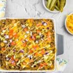 Cheeseburger casserole in a baking dish with pickles and cheese in bowls nearby.