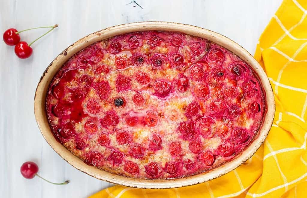 An oval baking dish with a baked cherry clafouti and a yellow towel.