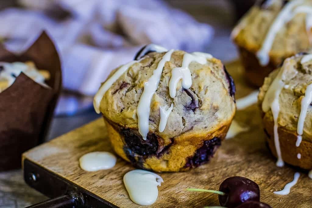 Cherry muffin drizzled with glaze on a wooden cutting board.
