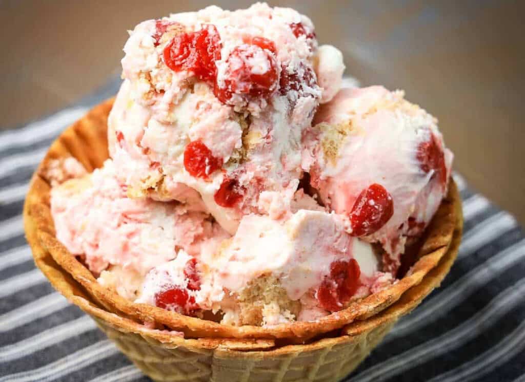 A waffle bowl of cherry ice cream on a striped towel.