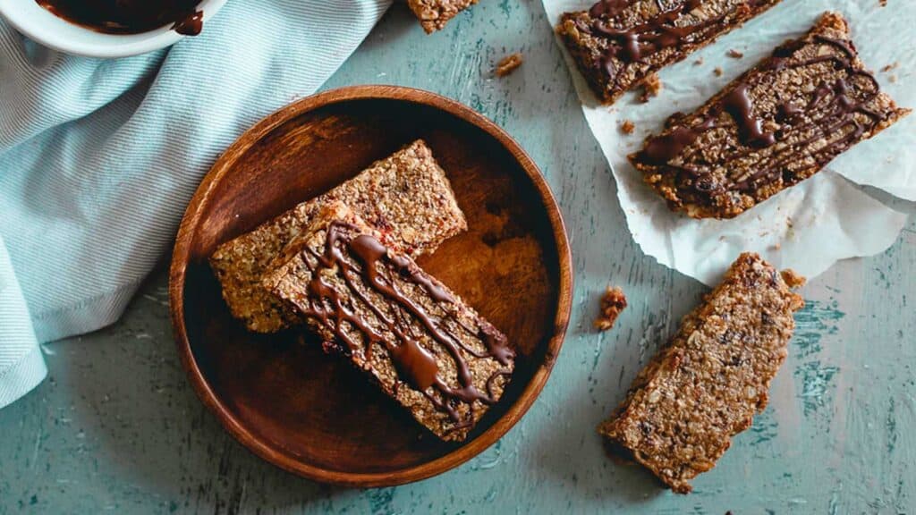 Cherry oat bars on a wooden plate with chocolate drizzle.