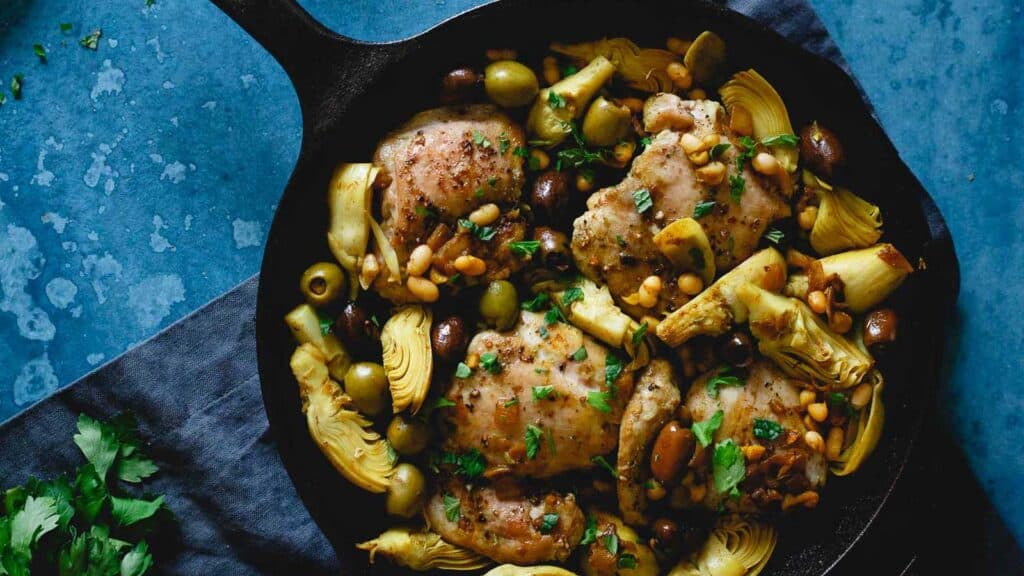 Chicken and artichokes with olives in a cast iron skillet.