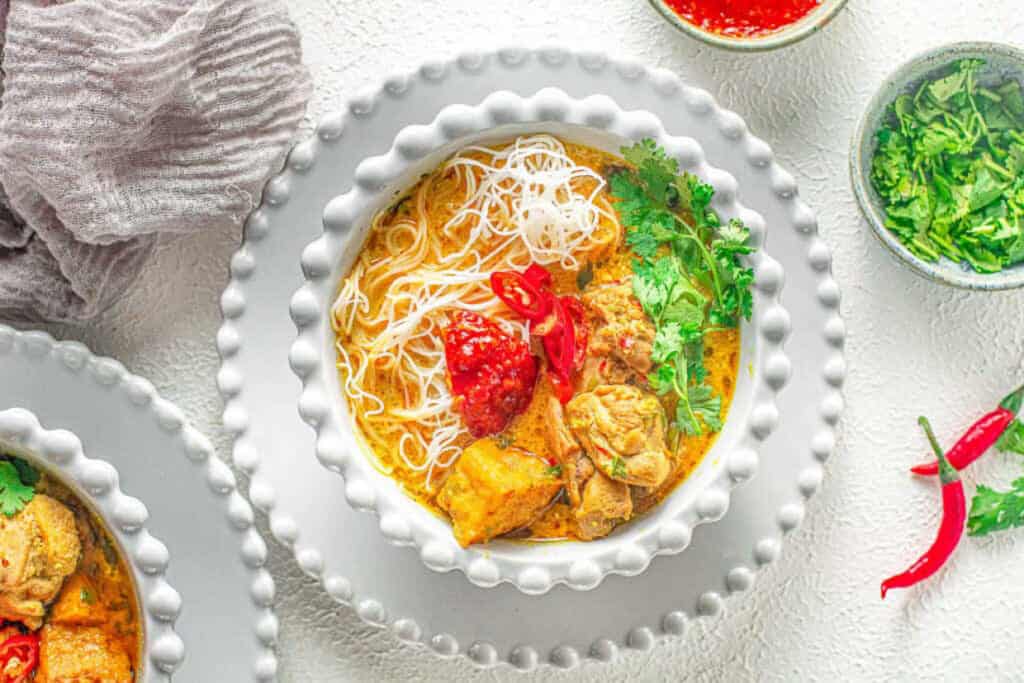 Overhead shot of chicken curry laksa in a white bowl.