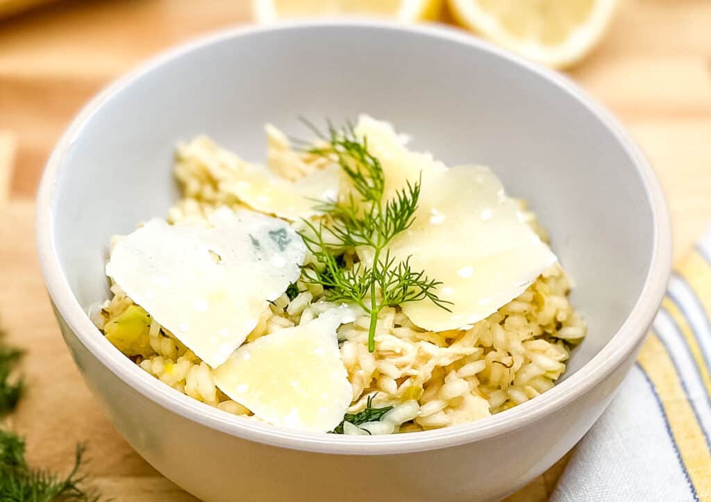 Chicken and leek risotto in a white bowl garnished with fresh dill and parmesan cheese.