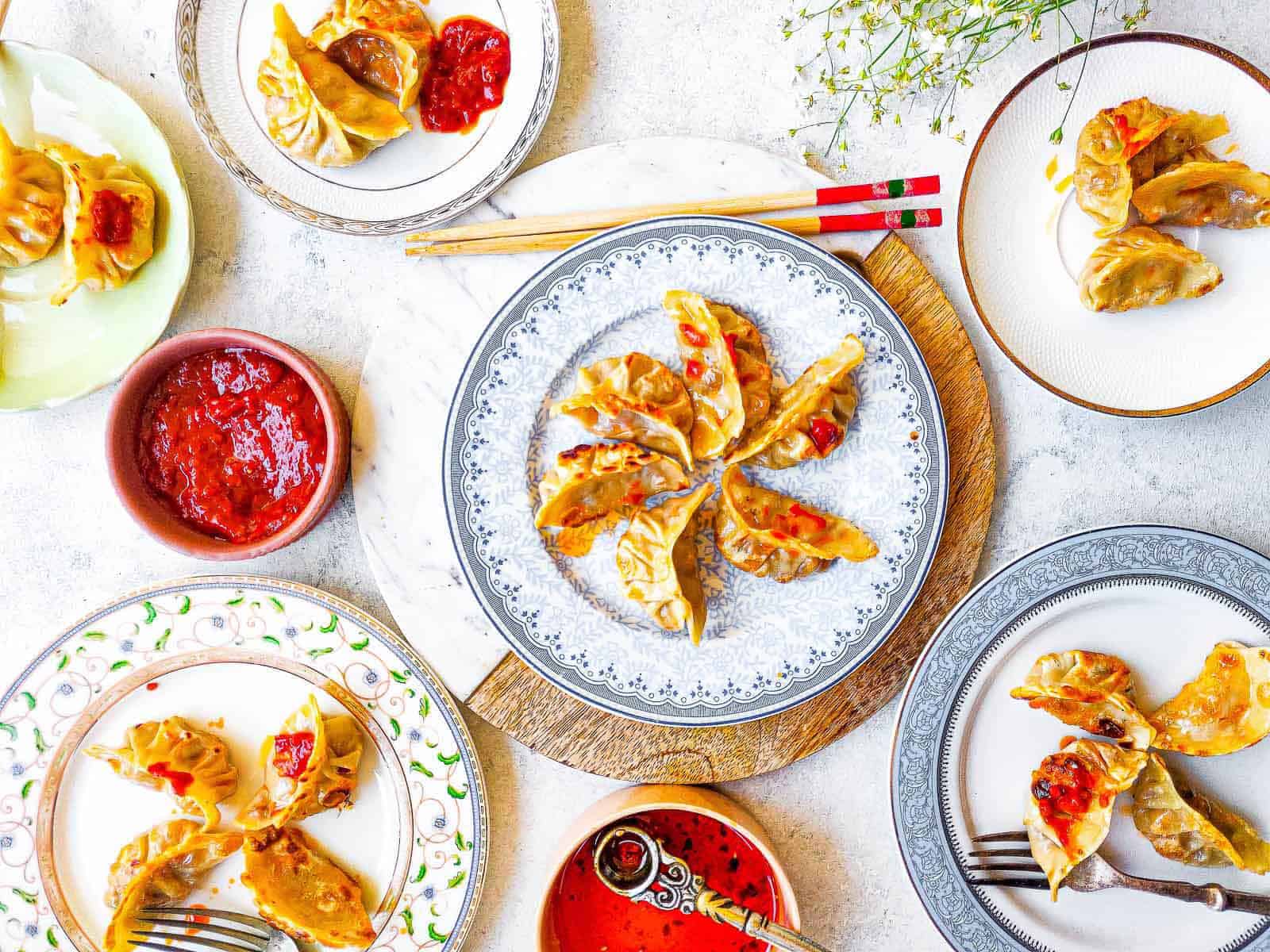 Overhead shot of chicken potstickers with chile paste on plates.