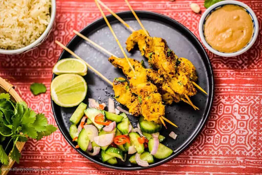 overhead shot of thai chicken satay on a black plate with peanut sauce on the side.