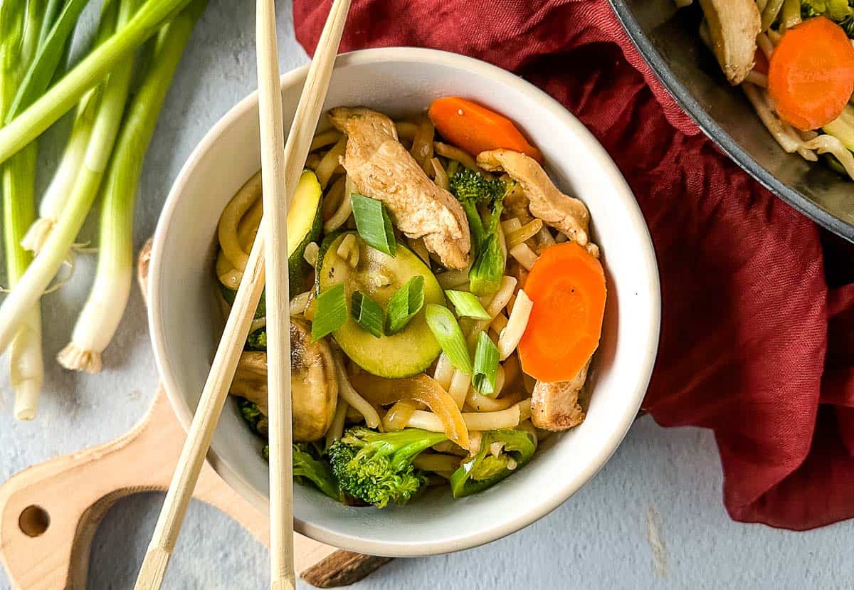 chicken yaki udon in a white bowl with chopsticks.