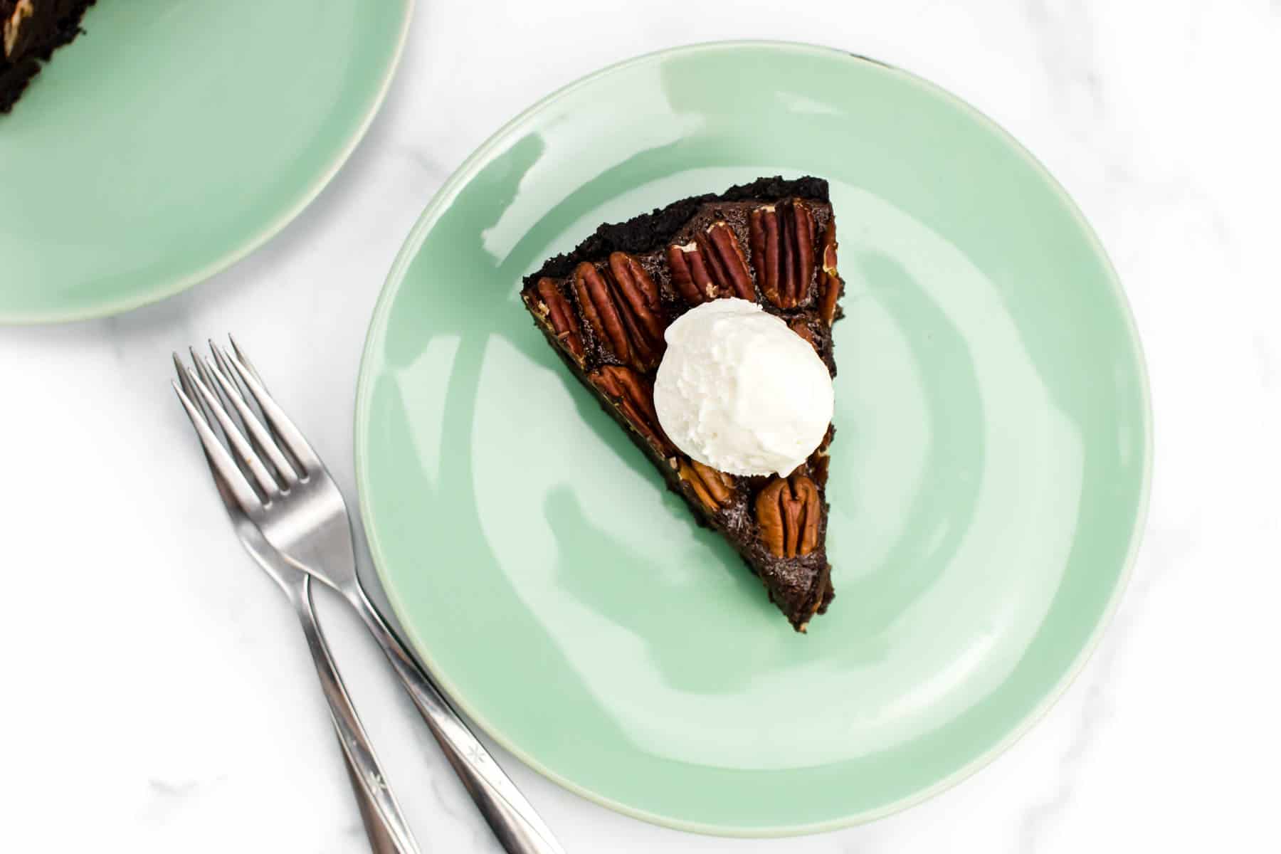 A chocolate pie with nuts on top and a scoop of ice cream on a light green plate with two forks.