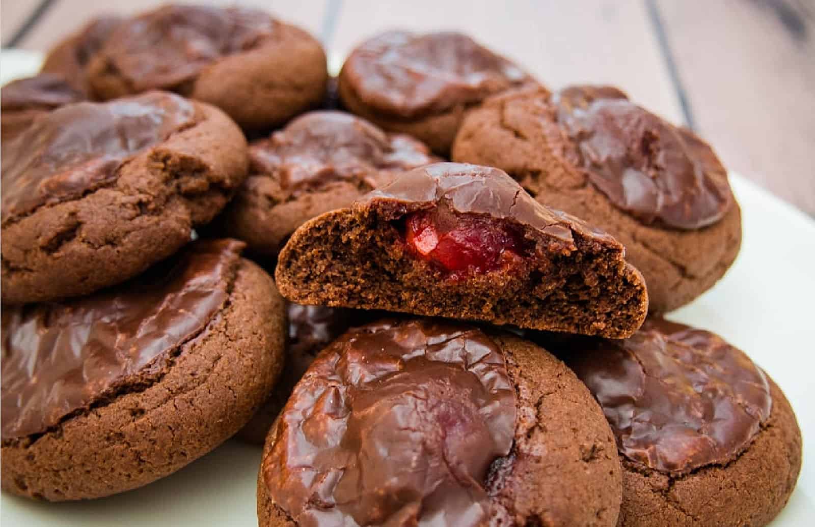 Plate of chocolate cookies with icing with one cut open to show the cherry inside.