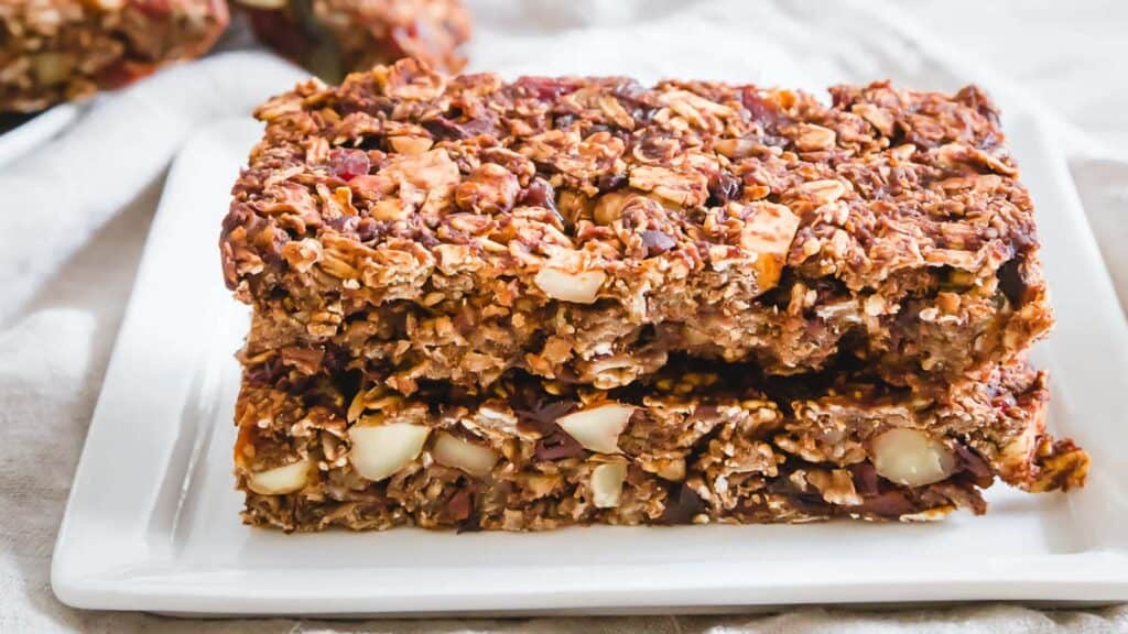 Homemade chocolate granola bars stacked on a white plate.