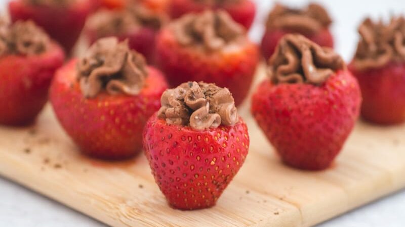 Chocolate cheesecake stuffed strawberries sprinkled with chocolate shavings and arranged on a cutting board.
