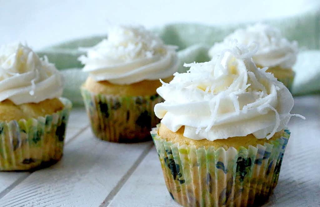 Frosted coconut cupcakes on a white board.