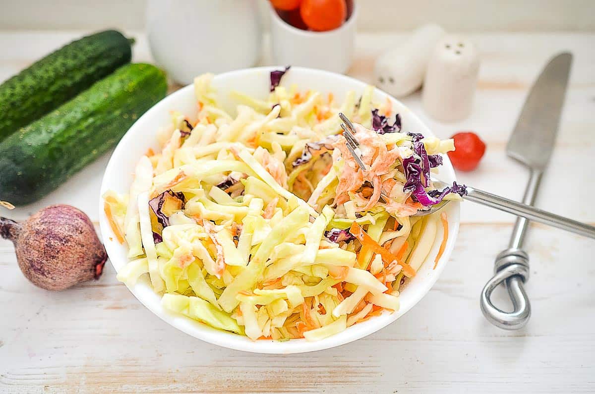 A bowl of coleslaw with vegetables and a fork.