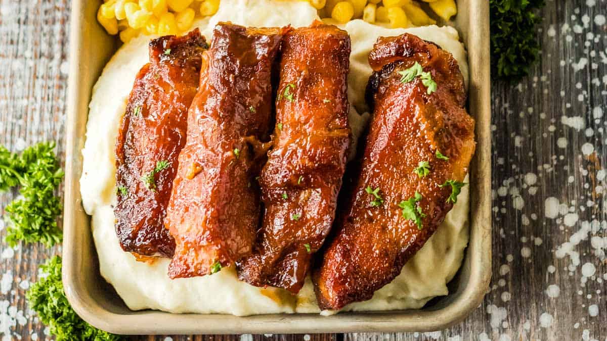 Slow cooker country style ribs on a tray on top of mashed potatoes with corn.