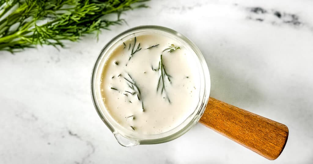 creamy dill sauce in a small glass pitcher with a wooden handle.
