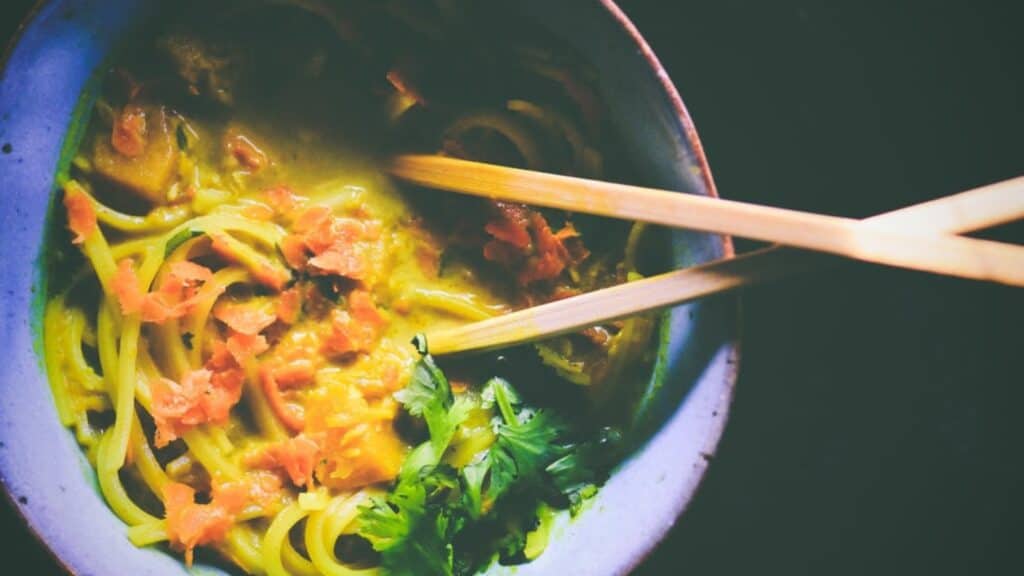 Close shot of a ceramic bowl filled with noodles in a yellow broth.