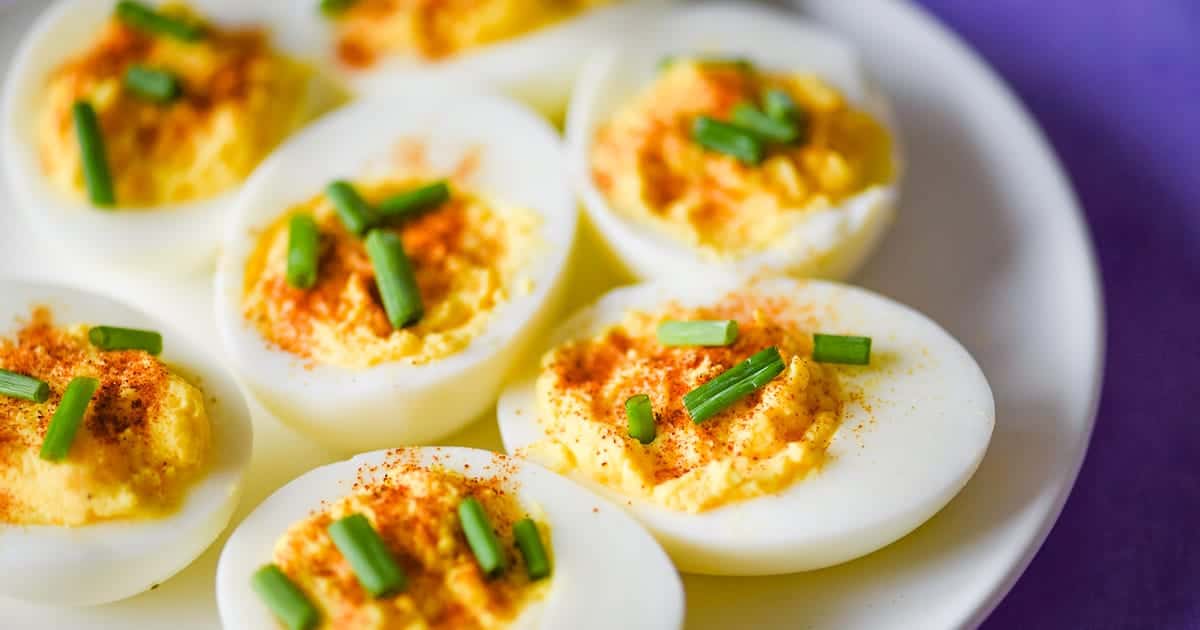 closeup shot of deviled eggs without mustard topped with snipped chives and paprika on a white plate.