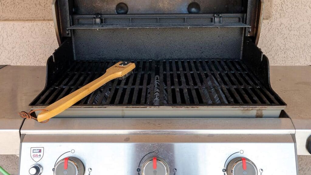 A gas grill with an open lid and a grill cleaning brush resting on the grate, illustrating how to clean a grill after a barbecue.