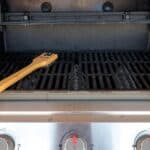 A gas grill with an open lid and a grill cleaning brush resting on the grate, illustrating how to clean a grill after a barbecue.