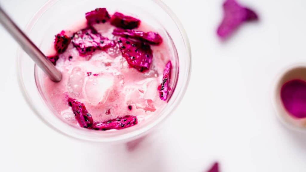 Top view of a tall glass filled with a pink drink filled with freeze-dried dragonfruit pieces.