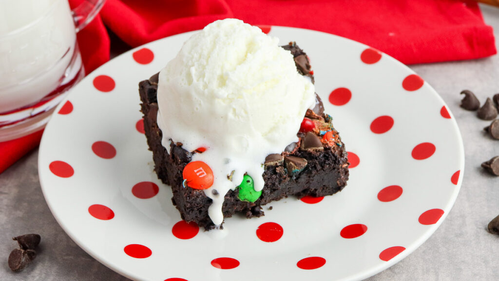 Chocolate dump cake topped with M&Ms and chocolate chips on a red and white plate with a scoop of ice cream.