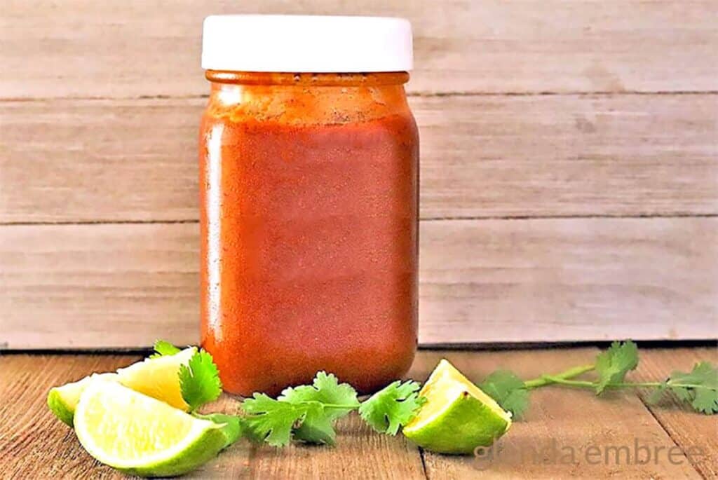 Homemade Enchilada Sauce in a mason jar on a wooden table with limes and cilantro.