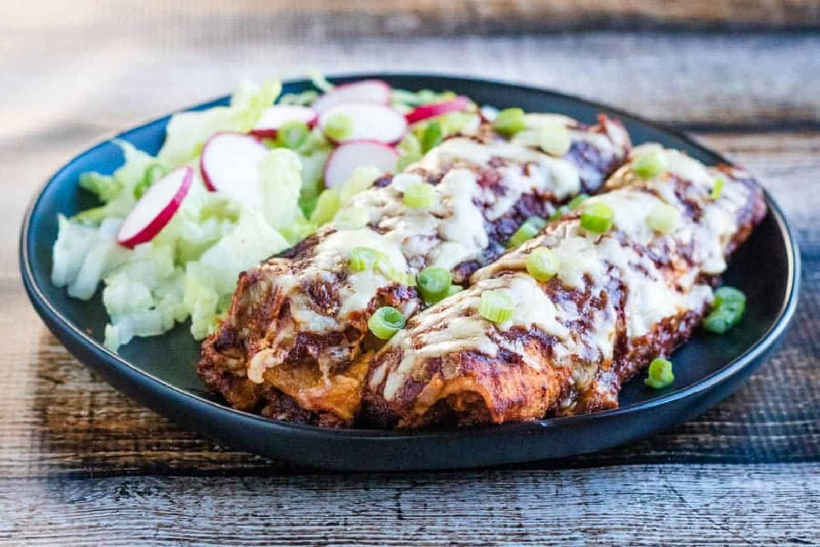 Low angle shot of chicken enchiladas on a plate with salad.