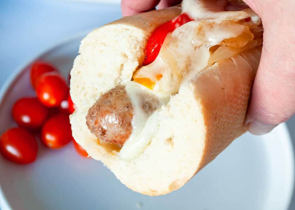 A bread roll with sausage and peppers being held in a hand
