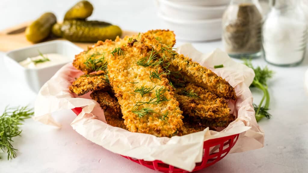 Red basket full of air fryer fried pickles with pickles in the background.
